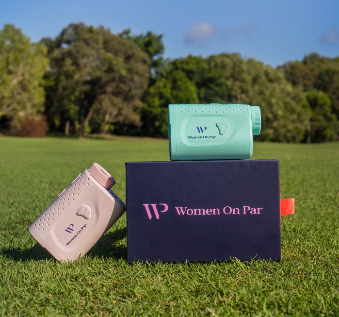Two golf rangefinders on a box with 'Women On Par' branding on a grassy field.